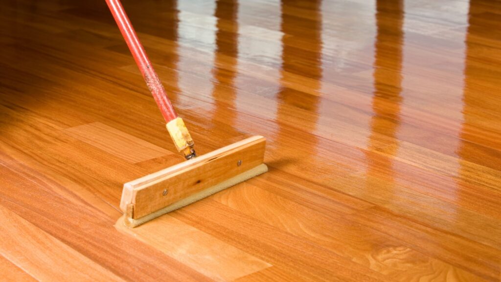 squeegee style brush applying polyurethane coating to a hard wooden floor