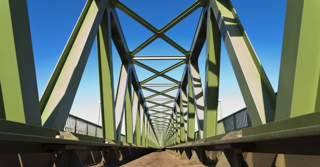 Metal structure of a large green bridge with blue skies in background