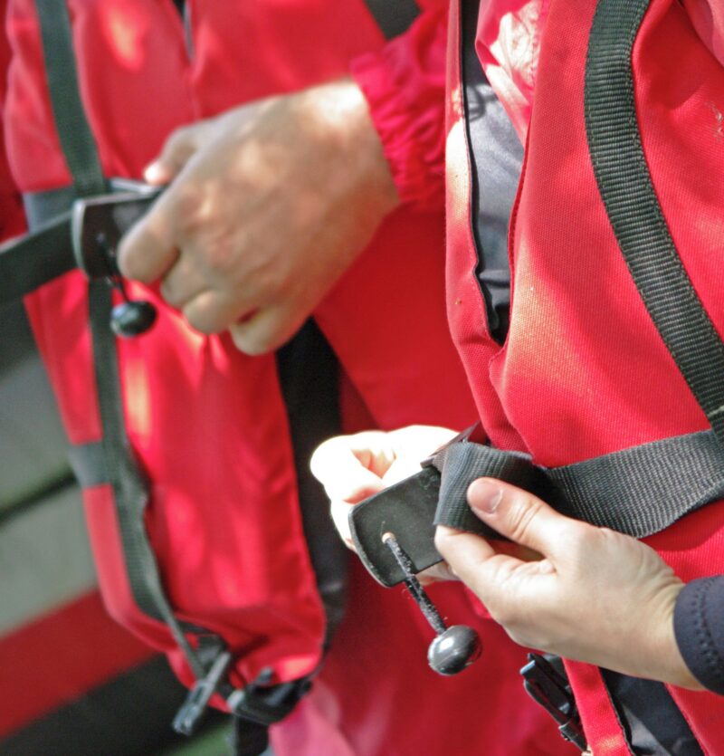 Two people fastening up red and black life jackets
