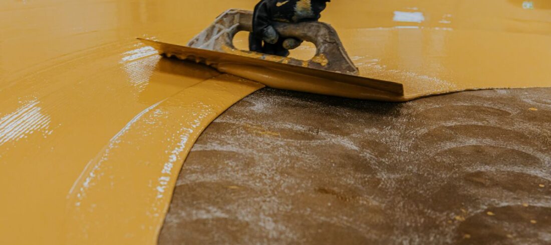 Yellow floor coating being applied using a large trowel.