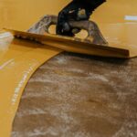 Yellow floor coating being applied using a large trowel.