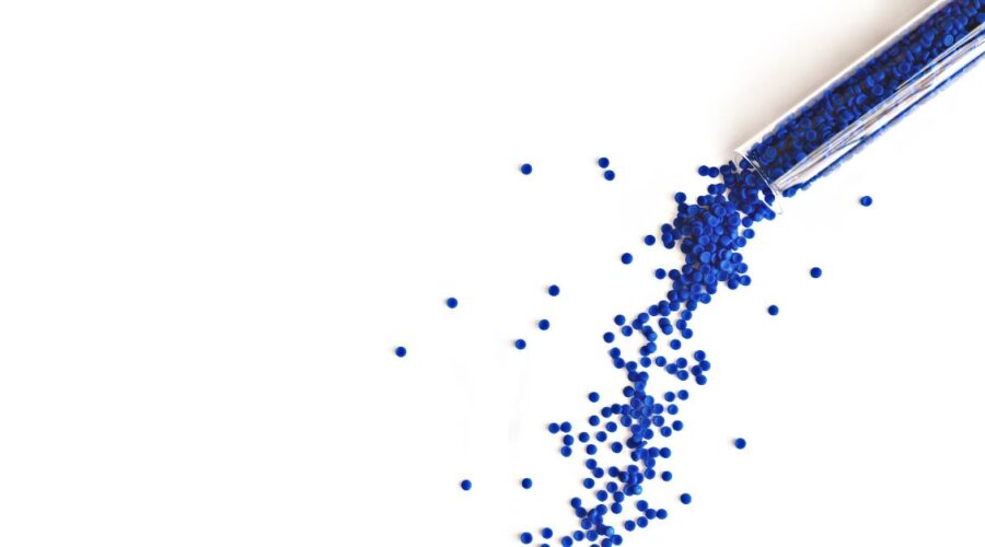 Blue polymer pellets being poured out of a test tube on a white background.