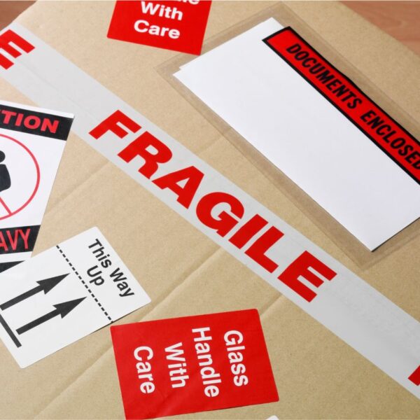 cardboard box with a variety of tapes and labels on top stating "fragile" and "handle with care"