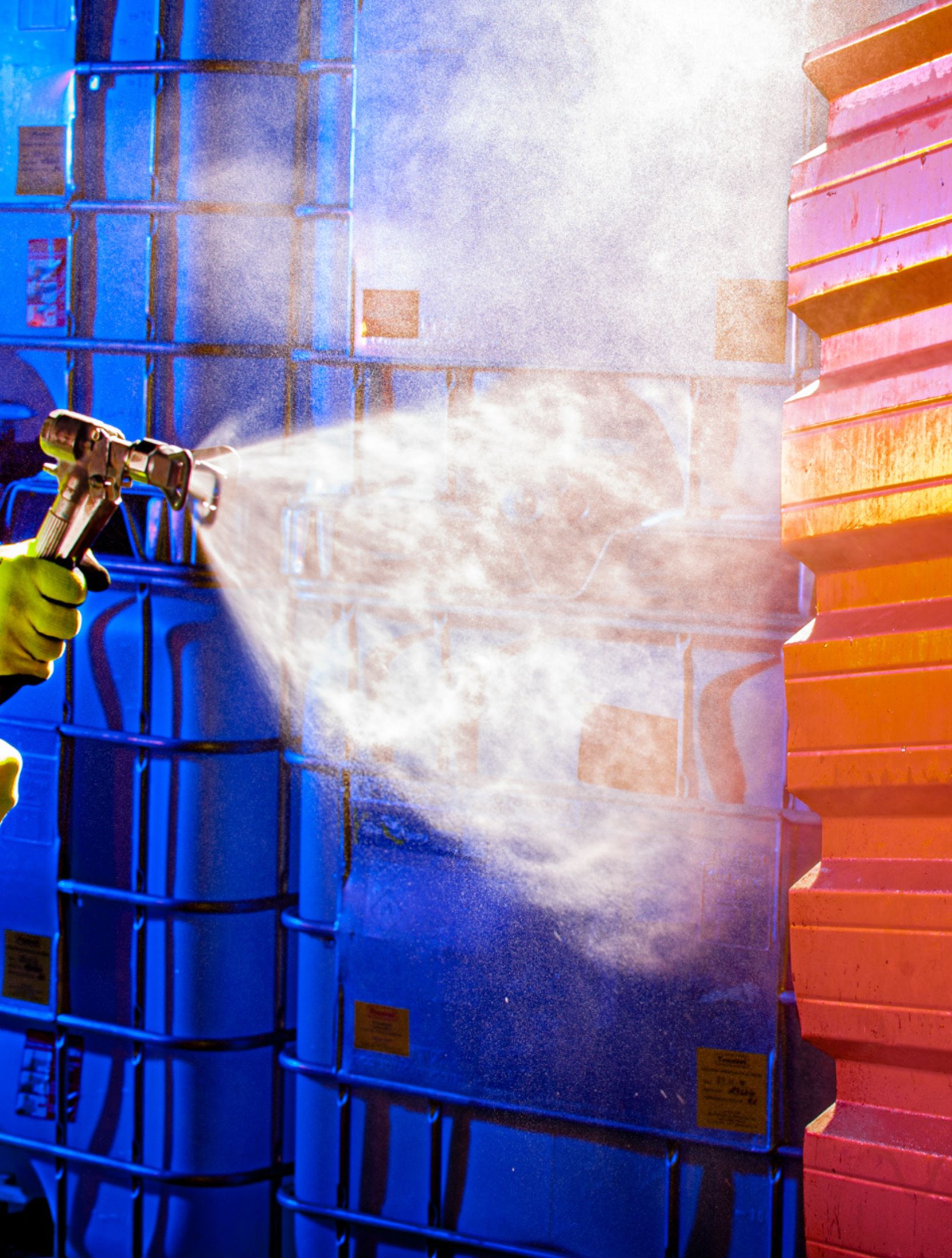 Someone using spray machine to apply a high performance coating to orange metal cladding.