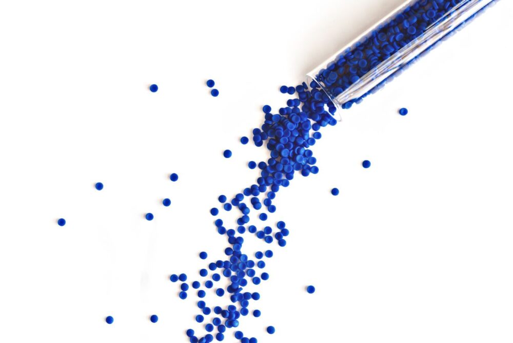 Blue polymer pellets being poured on to a white surface out of a test tube.