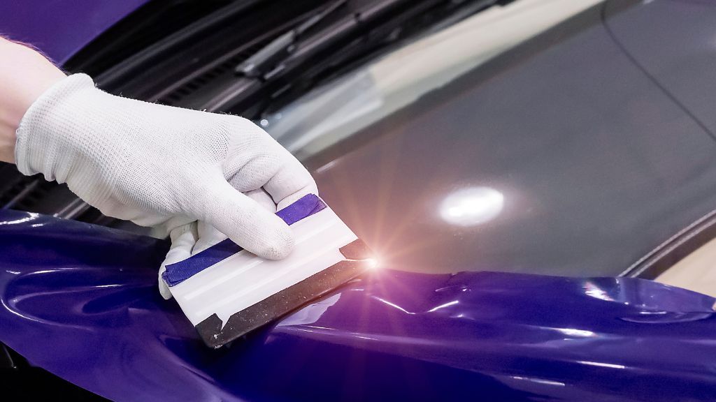 Purple wrap being applied to a car using pressure sensitive adhesive coating.